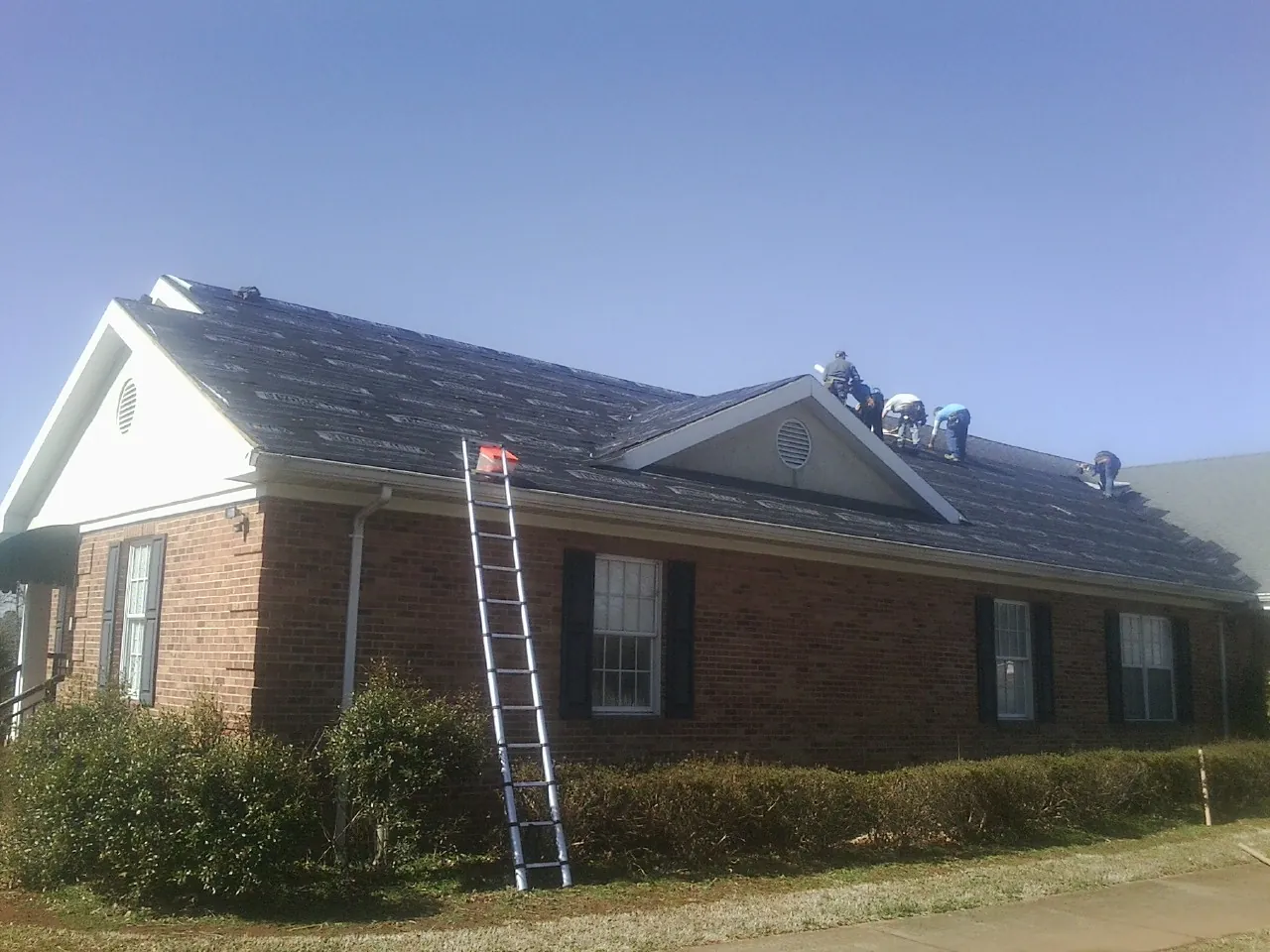 Crew tearing shingles off a brick ranch roof with a ladder set — Metal Roof Repair work by our crew in Springfield Gardens