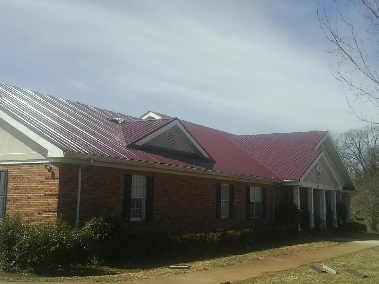 Red metal roof with gabled entries on a long brick building, from a Hail Damage Roof Repair job in Springfield Gardens