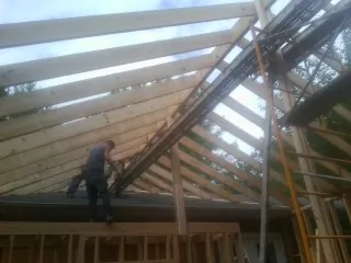 Rafters going up over a new addition with a worker on the wall in Springfield Gardens
