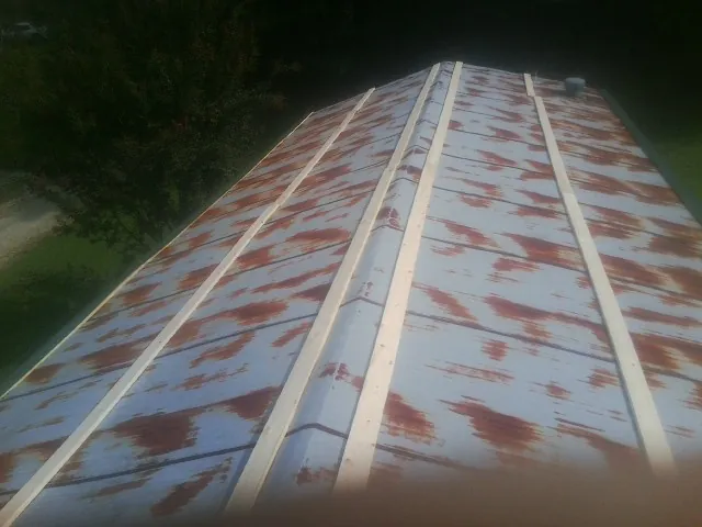 Rusted metal roof panels with new wood purlins before replacement — Storm Damage Roof Repair in Springfield Gardens by Roofing Brothers