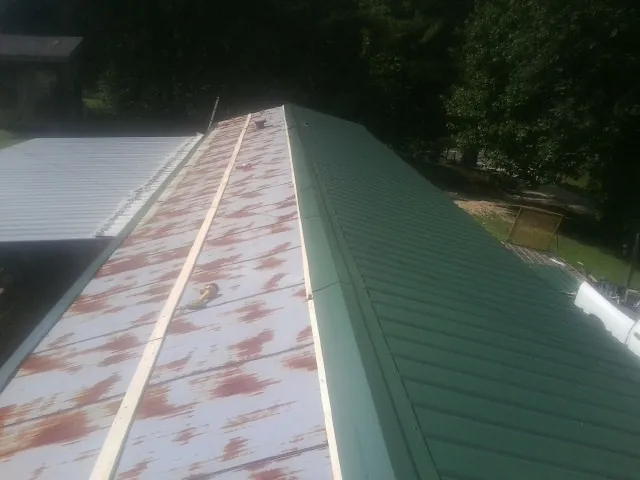 Old rusted panels beside newly installed green metal roofing — Wind Damage Roof Repair by Roofing Brothers in Springfield Gardens