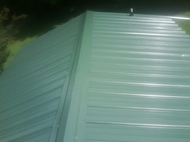 New green metal panels meeting at the ridge of a roof — Flat Roof Repair work by our crew in Springfield Gardens