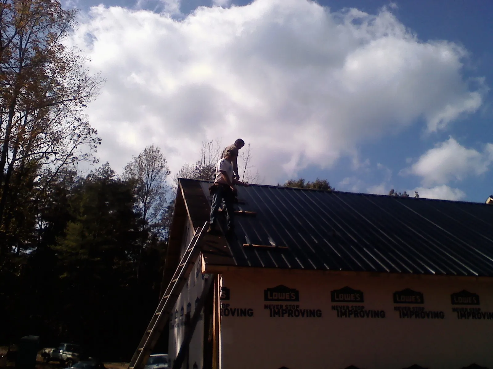 Roofer fastening dark metal panels high against a cloudy sky, from a Roof Inspection job in Springfield Gardens