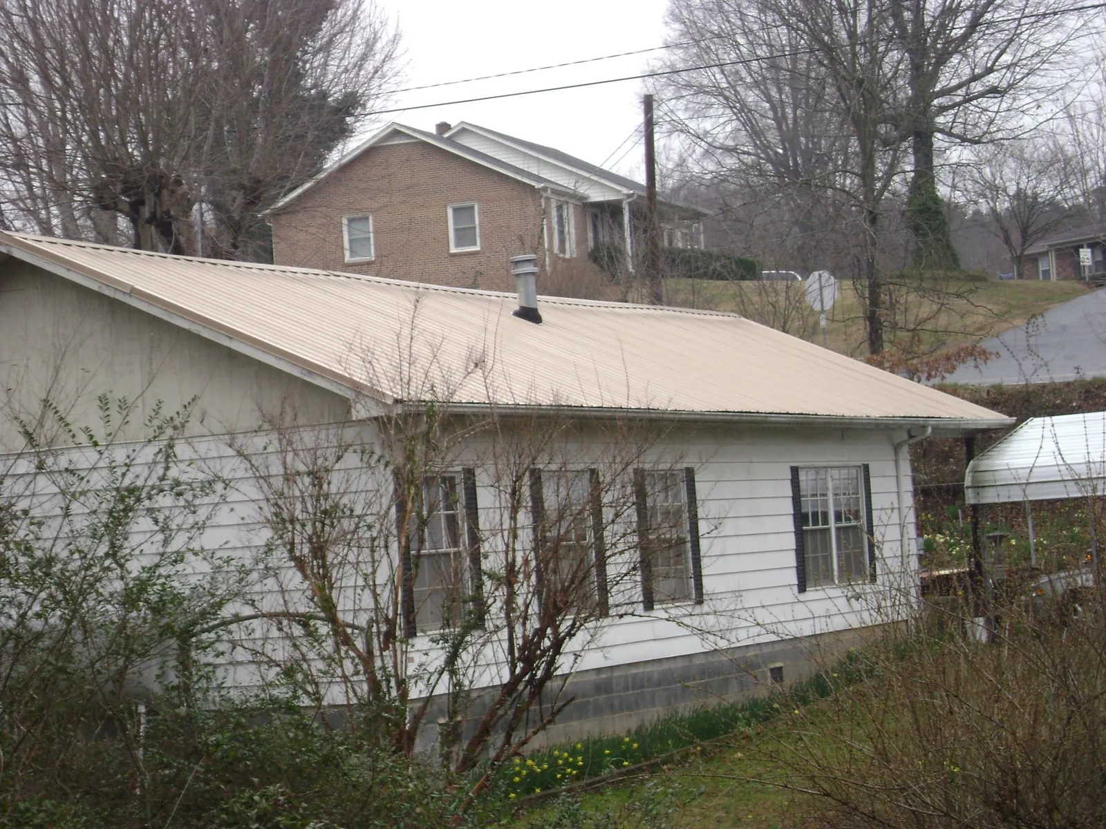 Tan metal roof on a white sided house set into a hillside — Commercial Roofing by Roofing Brothers in Springfield Gardens