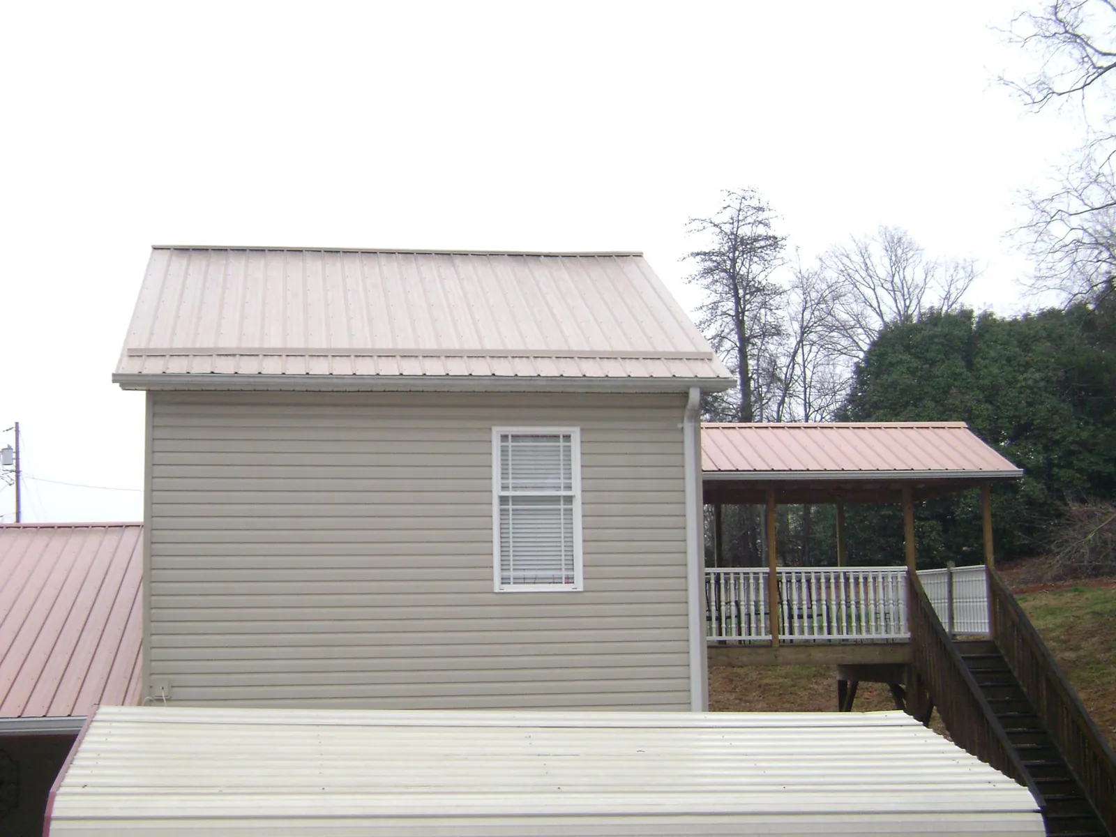 Tan metal roofs on a two story addition and attached porch, from a Roof Replacement job in Springfield Gardens